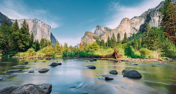 Rustige rivier met rotsen, bomen en bergachtergrond.