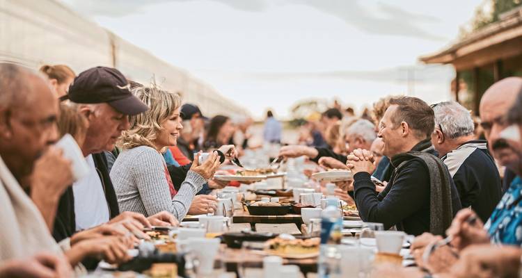 Große Gruppe speist im Freien neben einem Zug.