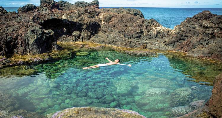 Person, die in einem natürlichen Felsbecken am Meer treibt.