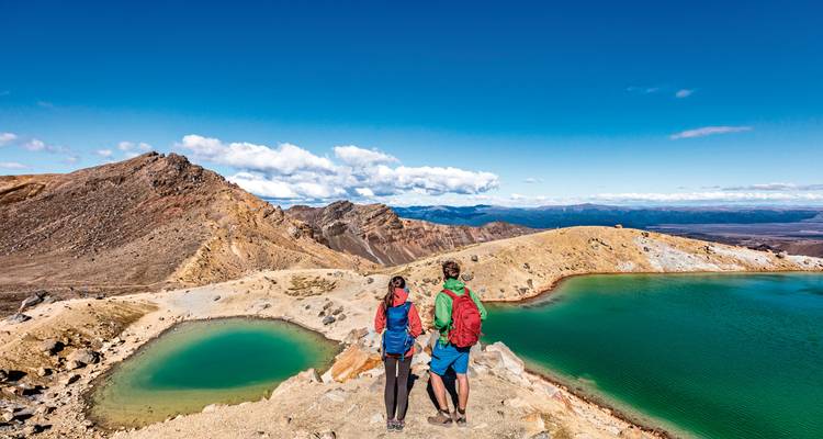 Dos excursionistas contemplando lagos coloridos y terreno montañoso.
