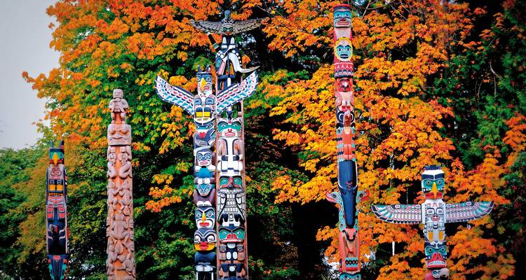 Totempfähle in einem Wald mit Herbstblättern.