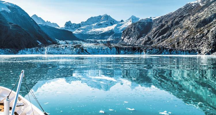 Une vue panoramique d'un glacier entouré de montagnes enneigées, avec un reflet dans l'eau calme.