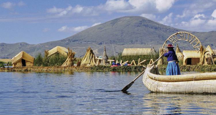 Menschen in traditionellen Schilfbooten auf einem See, mit Bergen im Hintergrund.