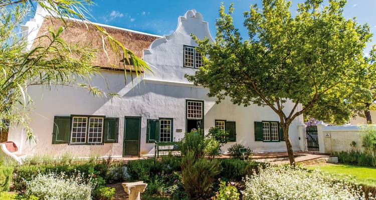 Koloniales Haus im niederländischen Stil, umgeben von Grün.