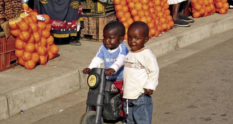 Twee kinderen bij een marktkraam met sinaasappels.
