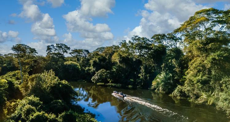 Riverboat cruising along a jungle river surrounded by forest.