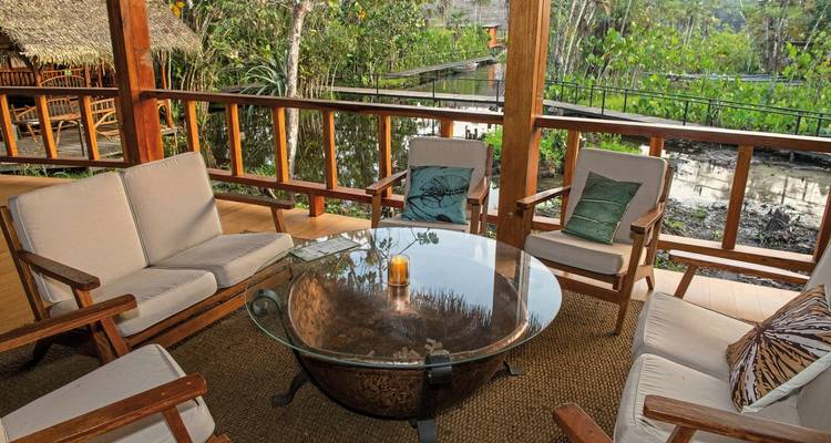 Un coin salon extérieur confortable avec des canapés et une table en verre entouré de verdure.