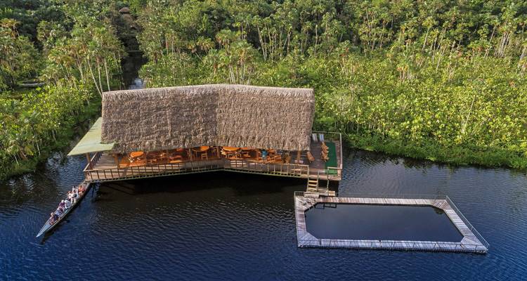 Une vue aérienne d'un lodge en bois entouré d'une végétation luxuriante et d'eau.