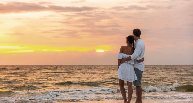 Couple se tenant sur le rivage regardant un coucher de soleil coloré sur des vagues douces