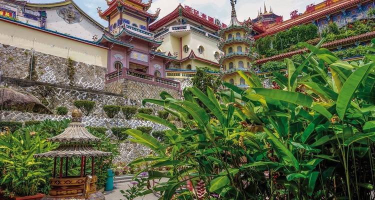 Elaborate temple facade with tropical vegetation in the foreground.