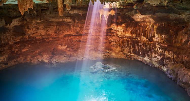Sonnenstrahl, der eine Cenote mit türkisfarbenem Wasser beleuchtet.