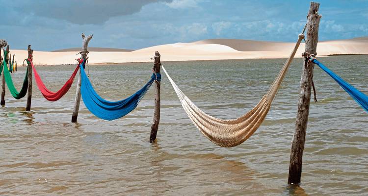 Hamacs au-dessus de l'eau avec des dunes de sable en arrière-plan.
