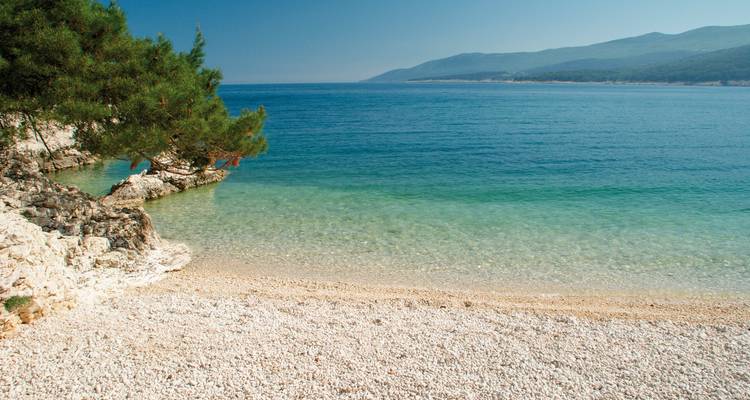 Ein steiniger Strand mit klarem Wasser und fernen Bergen.