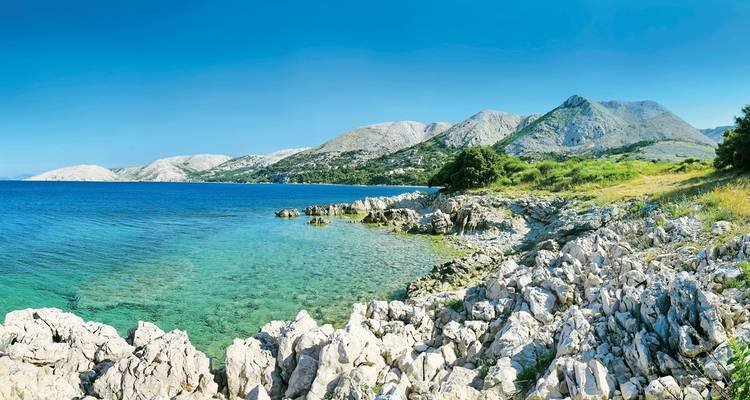 Eine felsige Küstenlinie mit klarem blauem Wasser und zerklüfteter Landschaft.
