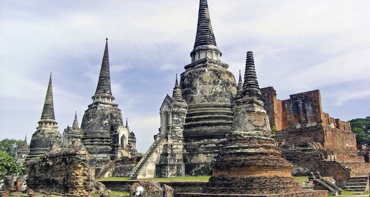 Oude Thaise ruïnes met prominente stupa's onder een bewolkte hemel.