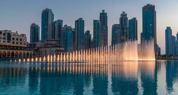 Stadtskyline mit beleuchteten Wasserfontänen in der Abenddämmerung.