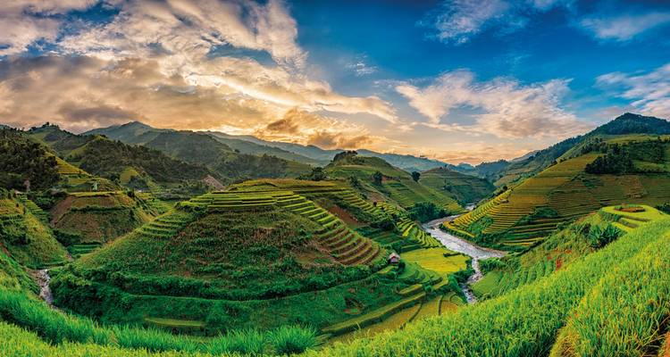 Uitgestrekte terrasvelden onder een lucht met dynamische wolkenpatronen.