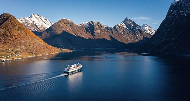 Cruiseschip dat door een fjord navigeert omringd door met sneeuw bedekte toppen.
