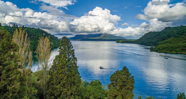 Blick über einen malerischen See, umgeben von Wald und Bergen.