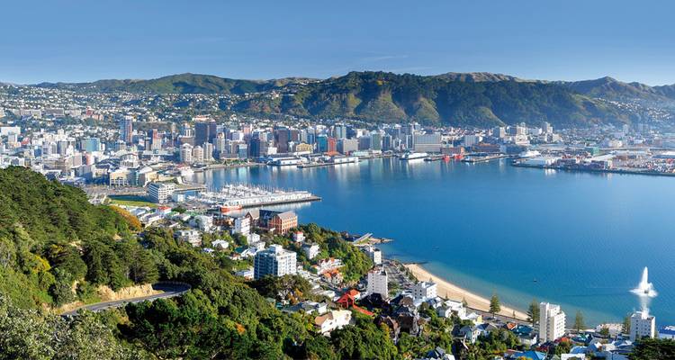 Luftaufnahme einer Stadt mit einer Uferpromenade und Hügeln im Hintergrund.
