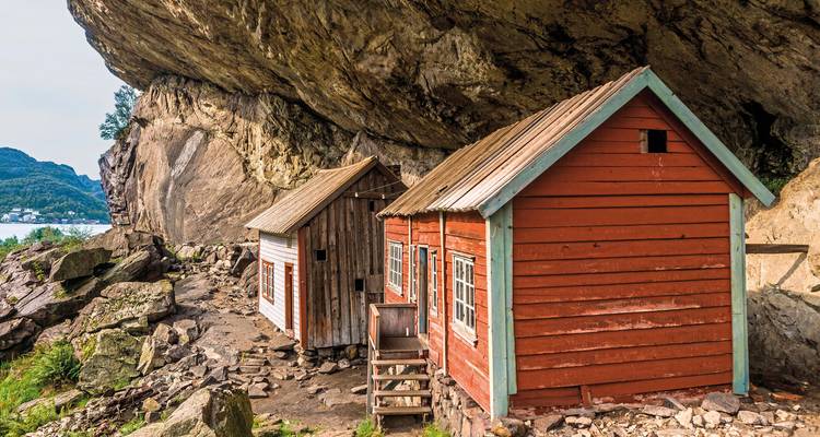 Two wooden cabins built against a rocky cliff.