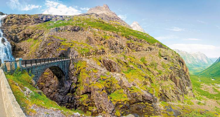 A mountain slope with a stone bridge and waterfall.