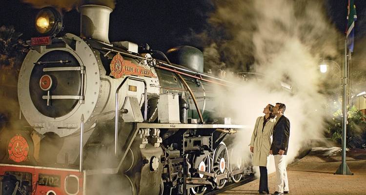 Un train à vapeur avec des personnes debout à côté de celui-ci la nuit.