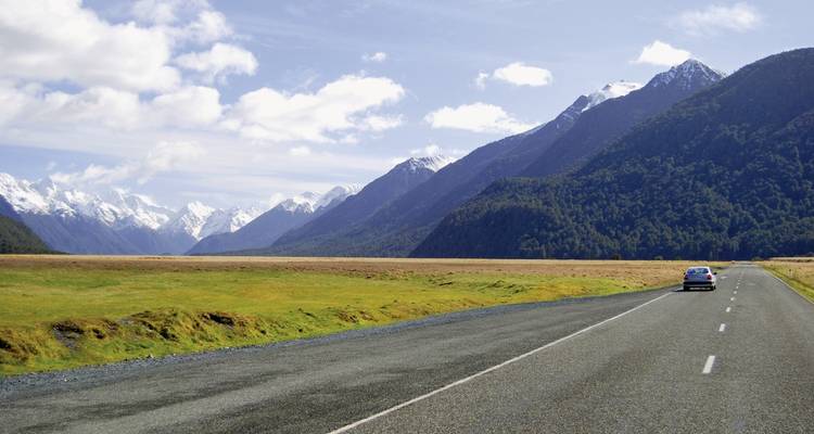 A road through a valley with snow-capped mountains in the distance.