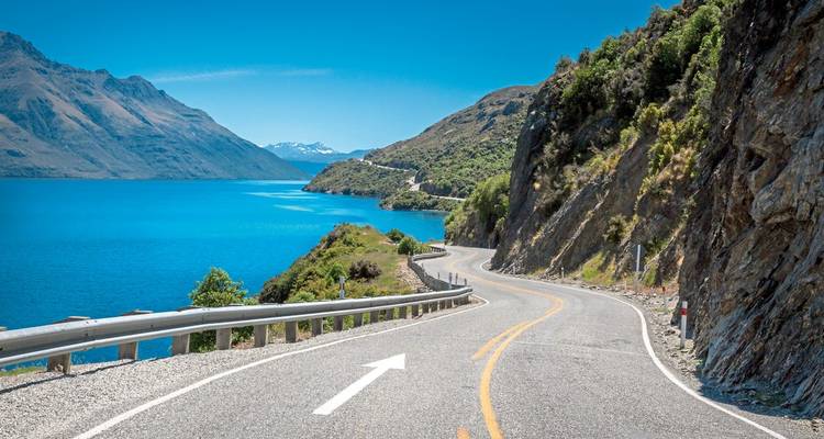 Scenic mountain road along a lake and forested hills.