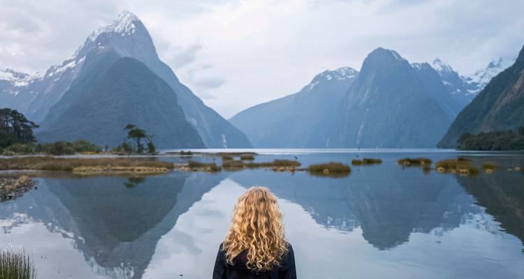 Back view of a woman looking at a lake surrounded by towering mountains.