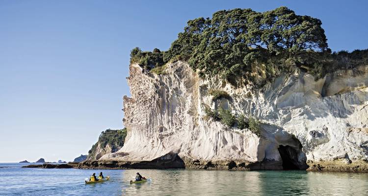 Kajakfahrer in der Nähe einer aufragenden Felswand mit klarem Wasser.
