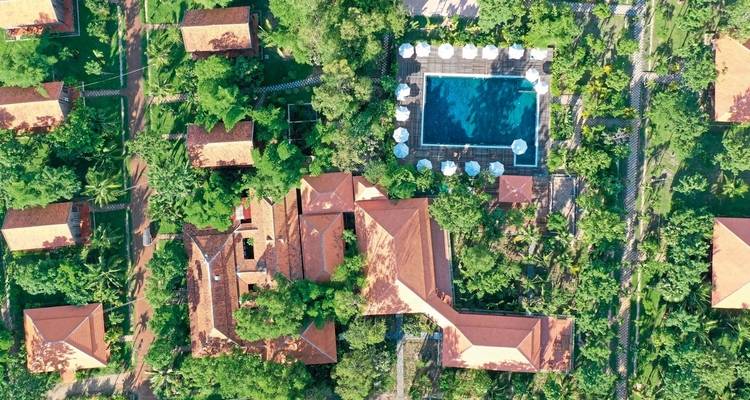 Aerial view of a resort with pool and multiple buildings nestled in greenery.