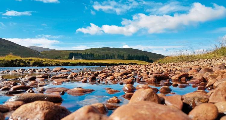 Rocky riverbank with vibrant water reflecting blue skies.