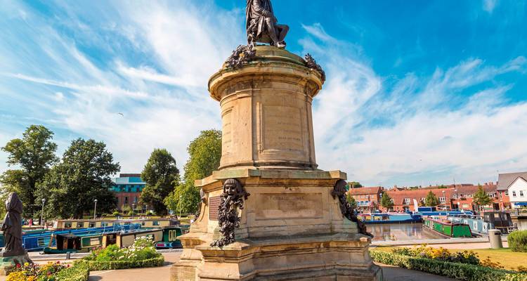 Statue in a park setting with a canal and boats nearby.