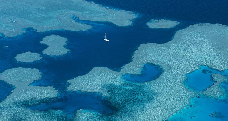 Aerial view of a boat in the middle of the ocean with clear blue water and coral formations.