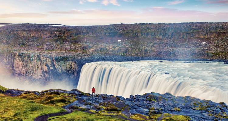 Majestic waterfall with rainbow and person standing near the edge.