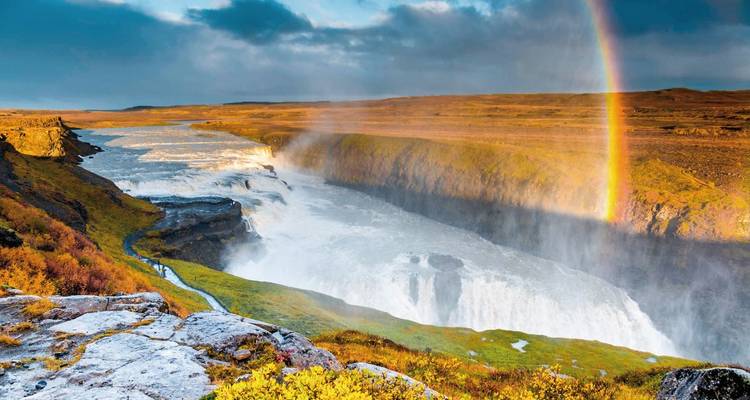 Un arc-en-ciel se dessine au-dessus d'une puissante cascade se jetant dans un profond ravin rocheux au cœur des hautes terres islandaises.
