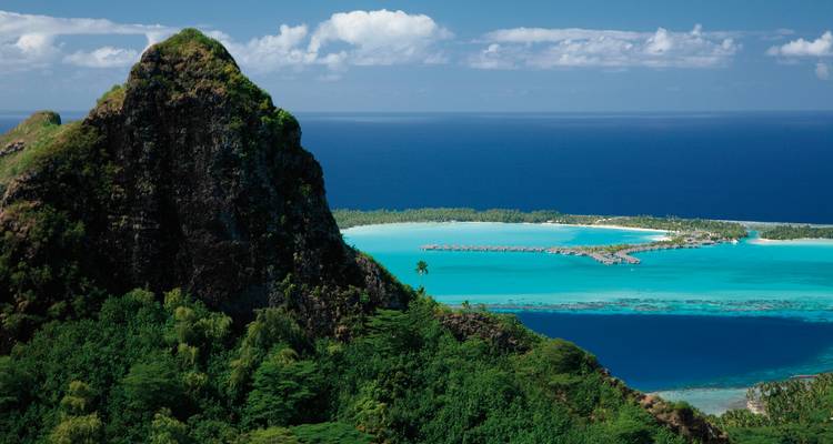 Vue panoramique sur le lagon depuis une colline avec des bungalows sur pilotis.