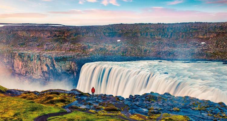 Toeschouwer die nabij de rand van Dettifoss staat terwijl watermassa's in een ruige kloof naar beneden storten.