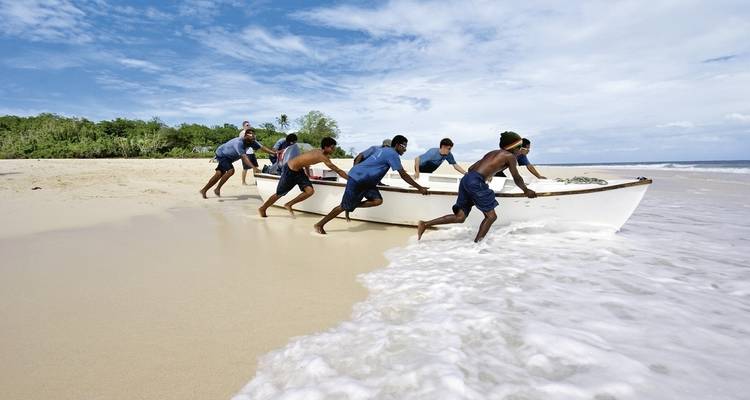 Groupe de personnes poussant un bateau dans l'eau sur une plage.