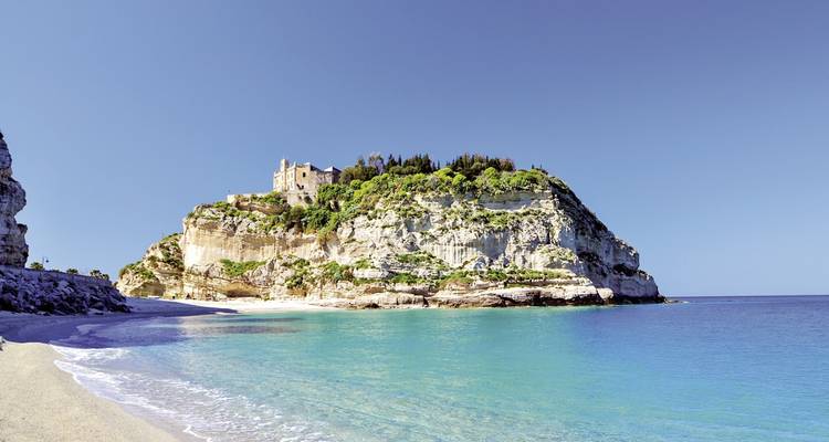 Una playa con acantilados y un edificio histórico en el promontorio.