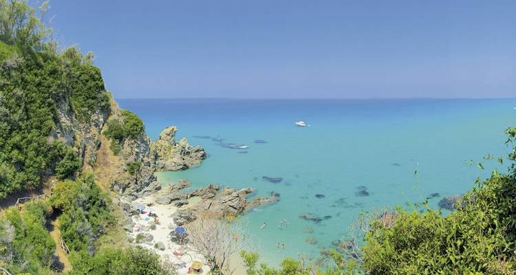 Vista panorámica de una playa con aguas turquesas y acantilados rocosos.