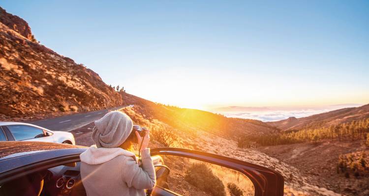 Person, die bei Sonnenaufgang aus einem Auto heraus Fotos in einer Berglandschaft macht.