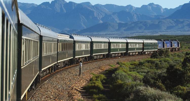 Trein die door schilderachtig landschap slingert met bergen op de achtergrond.