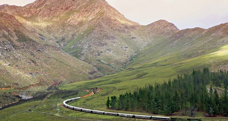 Trein die door een dramatisch berglandschap rijdt.