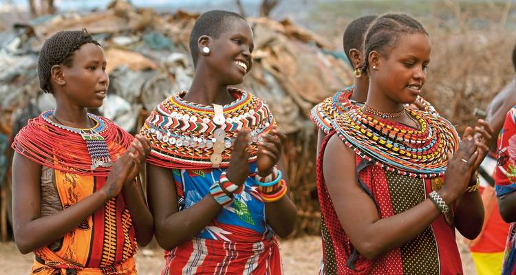 Eine Gruppe von Maasai-Frauen in traditioneller Kleidung, die klatschen und lächeln.