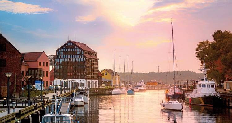 Sonnenuntergang über einem Kanal mit Booten und traditionellen Gebäuden.