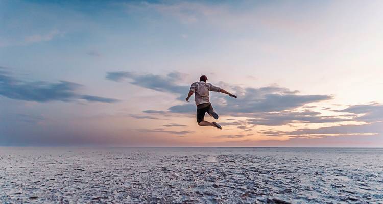 Personne sautant sur un vaste désert de sel au coucher du soleil.