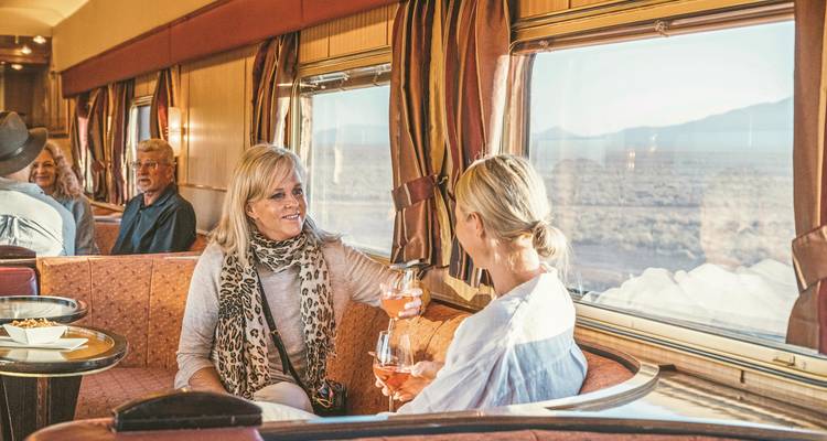 Gruppe von Menschen beim geselligen Beisammensein in einem Zugabteil.