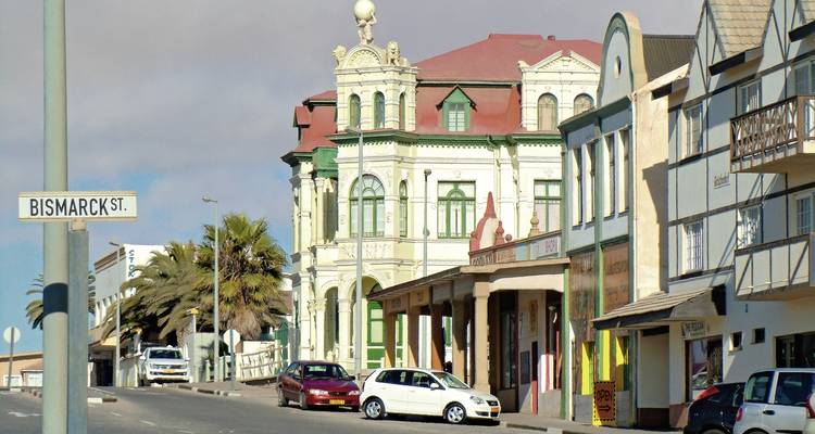 Historische Kolonialfassaden entlang der Bismarck-Straße mit geparkten Autos und Palmen in Swakopmund.